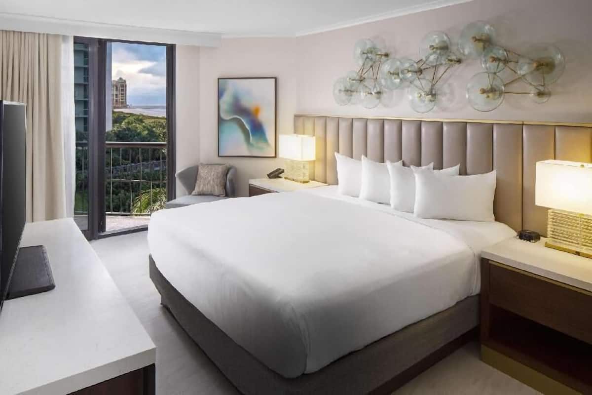 Een hotelkamer met een groot bed, een bureau, een stoel, een televisie en een balkon met uitzicht.