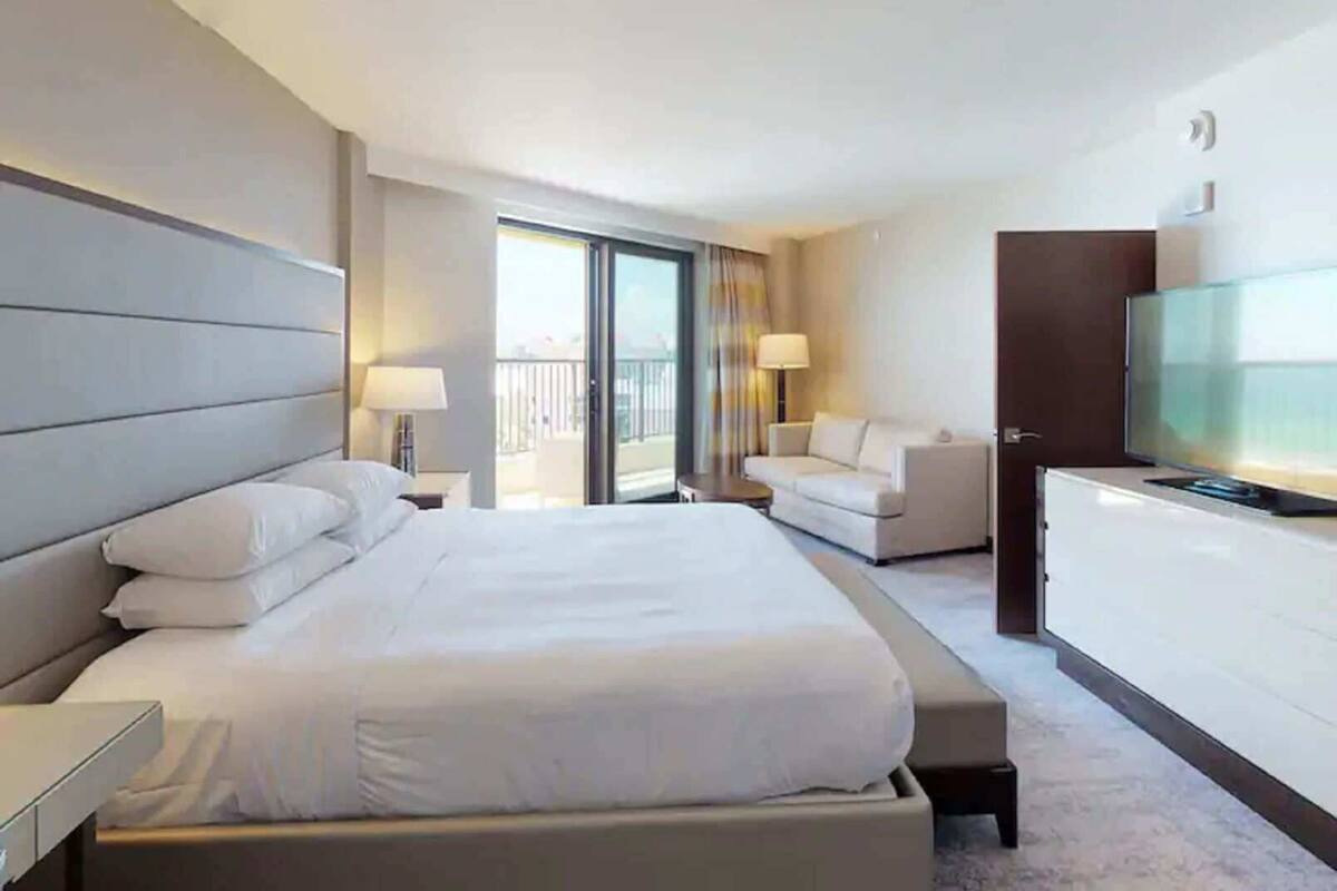 Een hotelkamer met een groot bed, een televisie, een bank, een bureau en een balkon.