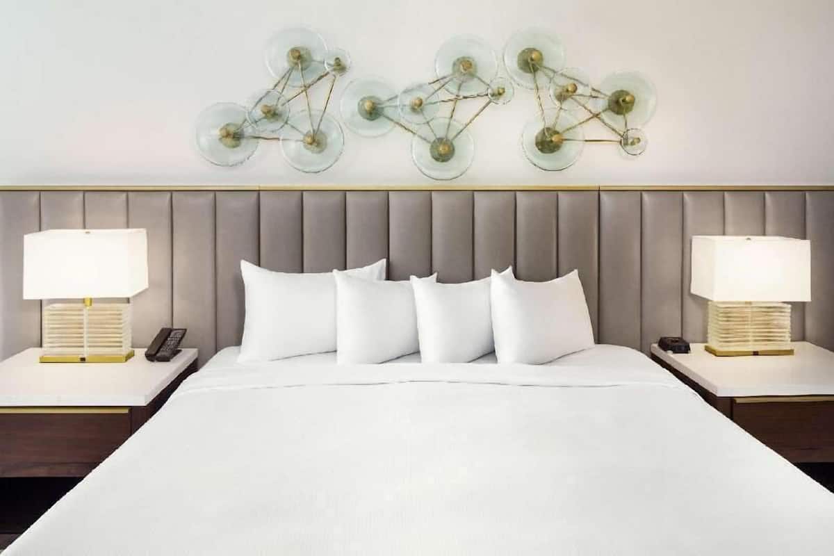 Een hotelkamer met een groot bed, twee nachtkastjes met lampen en een wandlamp.