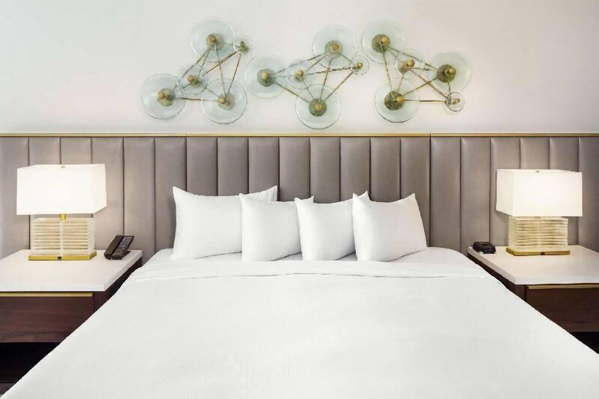 Een hotelkamer met een groot bed, twee nachtkastjes met lampen en een wandlamp.