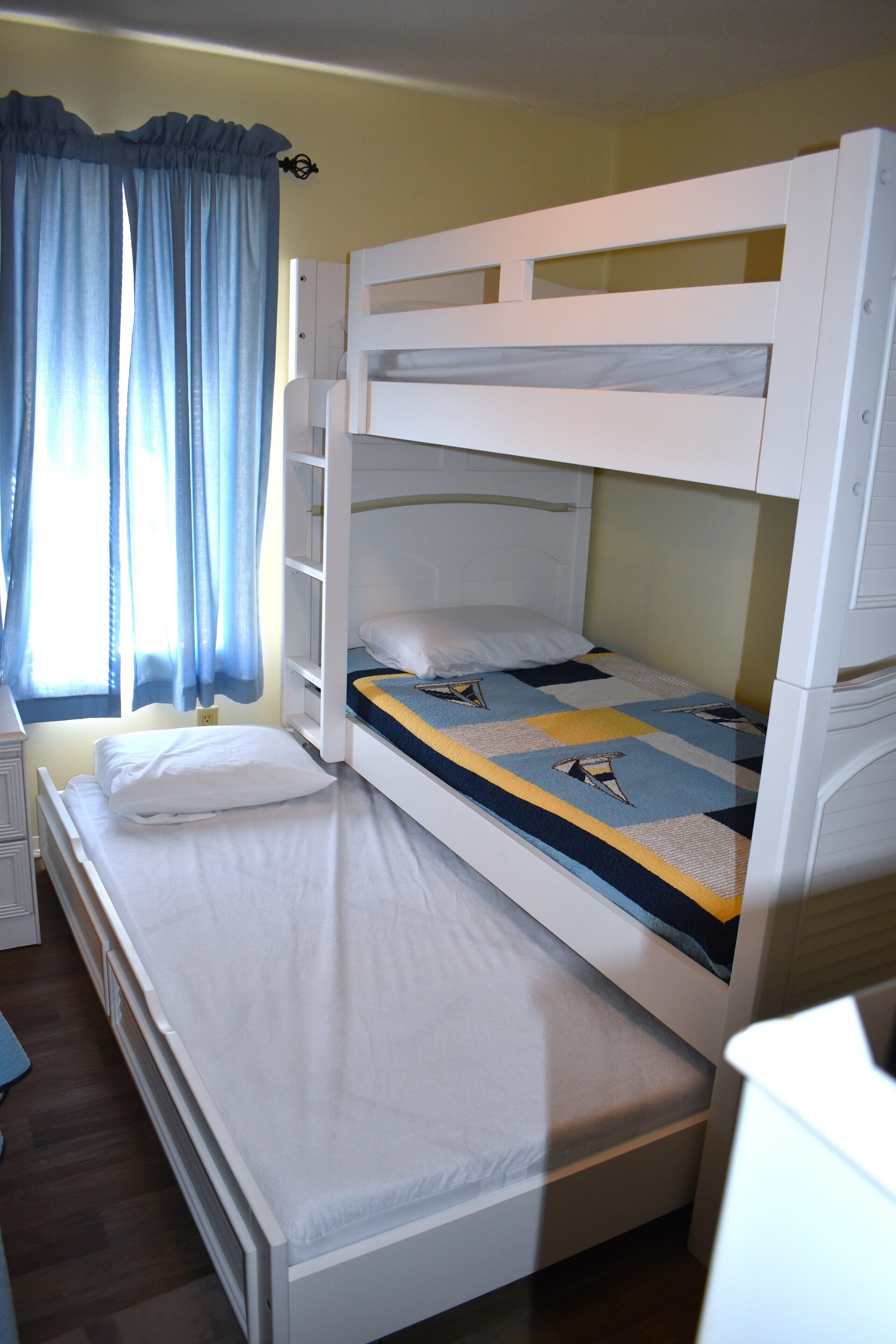 A bunk bed room with a window, curtains, and a bedside table.