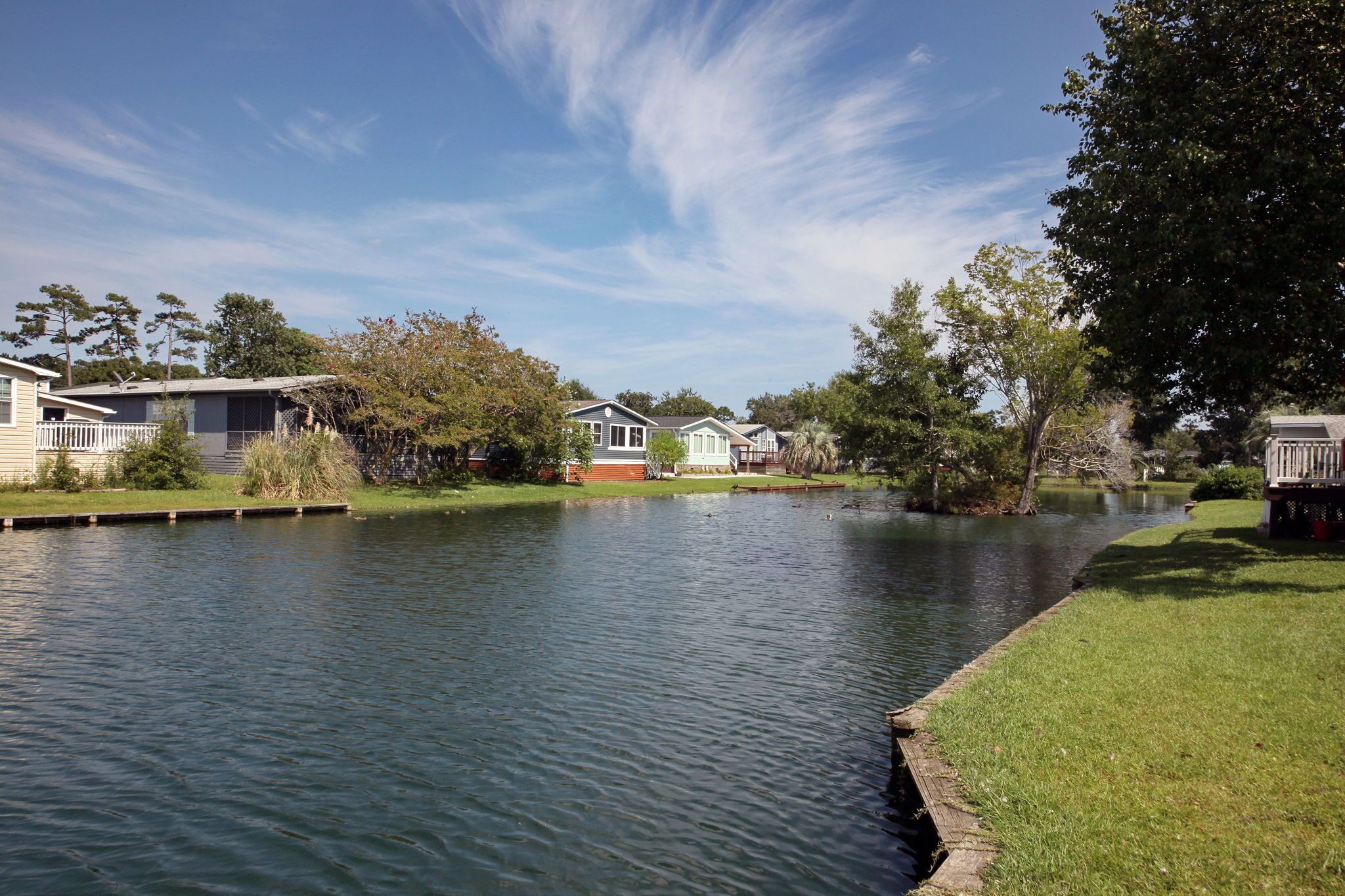 A calm lake with houses on the shore, surrounded by trees and clear skies.