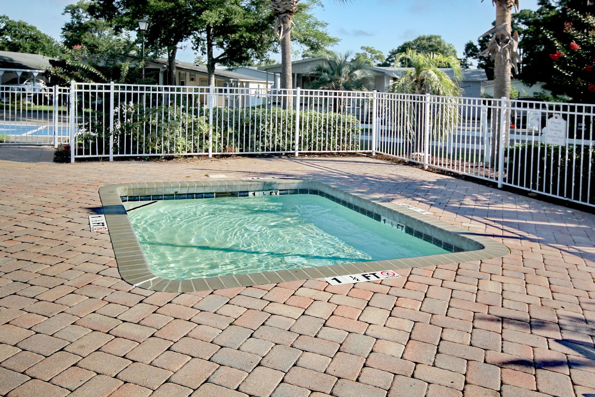 A rectangular pool with a brick border and a white fence surrounding it.
