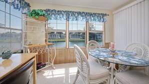 A dining area with a glass table, white wicker chairs, and a view of a lake through large windows. - Beach House with a lake.  (Surfside Beach)