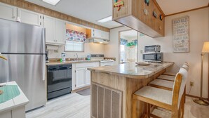 A modern kitchen with a stainless steel refrigerator, built-in oven, and microwave. There is a wooden island with bar stools, and a large window with a colorful curtain. - Beach House with a lake.  (Surfside Beach)