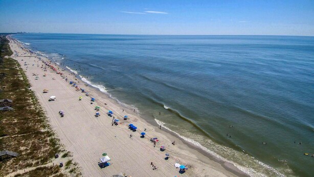 A beach with rows of umbrellas and beachgoers. - Beach House with a lake.  (Surfside Beach)