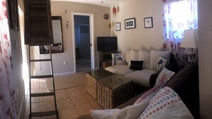 A living room with a sofa, a coffee table, a TV, and a wicker basket. - Charming Hidden Cottage (Los Gatos)