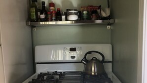 A kitchen with a stove, oven, and a shelf above containing various kitchen items. - Charming Hidden Cottage (Los Gatos)