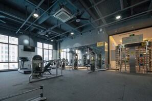 Une salle de sport équipée de divers appareils d’exercice, dotée de grandes fenêtres et d’un espace vestiaire.