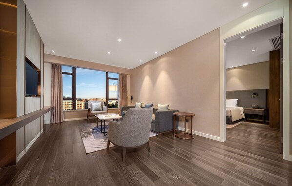 A modern living room with a sofa, armchair, and coffee table, large windows with a view, and a flat-screen TV mounted on the wall. - Holiday Inn Express Jinjiang Anhai by IHG (Quanzhou)