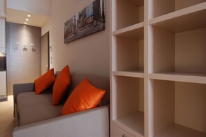 A modern living room with a sofa and orange cushions, a painting on the wall, and a white shelving unit.