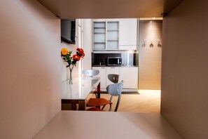 A compact kitchen with white cabinets, a microwave, and a dining area with a table and chairs.