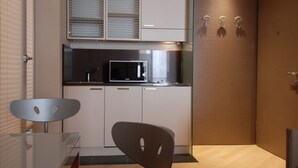 Ett modernt kök med vita skåp, en mikrovågsugn i rostfritt stål och ett bord i glas med en stol i metall.