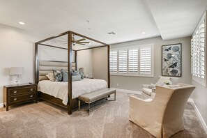 A four-poster canopy bed with a bench, a bedside table, and a chair in a bedroom with large windows and a ceiling fan. - Le Château at Las Palmas Resort - The nicest unit in the community!! (St. George)