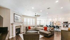 A spacious living room with a fireplace, a sectional sofa, and a dining area with a kitchen in the background. - Le Château at Las Palmas Resort - The nicest unit in the community!! (St. George)