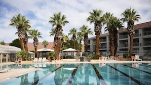 A swimming pool with lounge chairs and palm trees, surrounded by a building with balconies. - Le Château at Las Palmas Resort - The nicest unit in the community!! (St. George)
