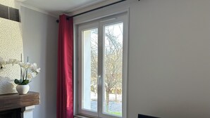 Une pièce avec un radiateur blanc, une cheminée et une fenêtre ornée d’un rideau rouge.