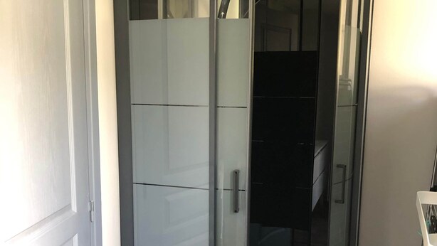 Un espace de douche d’angle avec une porte en verre, une porte blanche sur le côté gauche et un plancher en bois.
