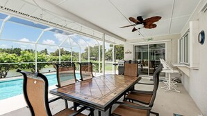 Un patio techado con piscina, mesa de comedor, sillas y ventilador de techo.