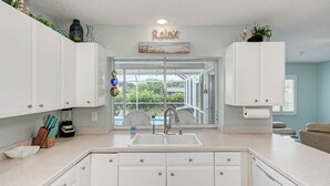 Una cocina moderna con armarios blancos, un lavamanos doble y vistas a una piscina a través de puertas de vidrio.
