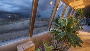 A room with large windows offering a view of a stormy landscape. - Spectacular Earthship (El Prado)