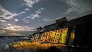 A modern building with large windows and a sloped roof, likely a hotel or resort, with a view of the sky and stars. - Spectacular Earthship (El Prado)