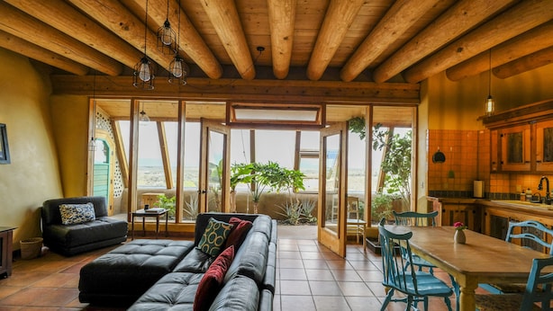 A spacious living area with a leather sofa, a dining table with chairs, and a kitchen area. - Spectacular Earthship (El Prado)
