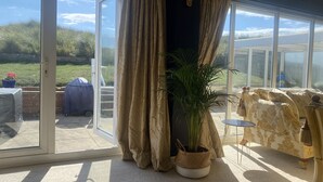 Une pièce dotée d’une porte-fenêtre coulissante donnant sur une terrasse, d’une plante en pot et d’un canapé recouvert d’un tissu à motifs.