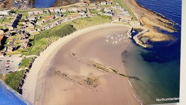 Vue aérienne d’une ville côtière avec une plage de sable, un port de plaisance et des immeubles résidentiels.