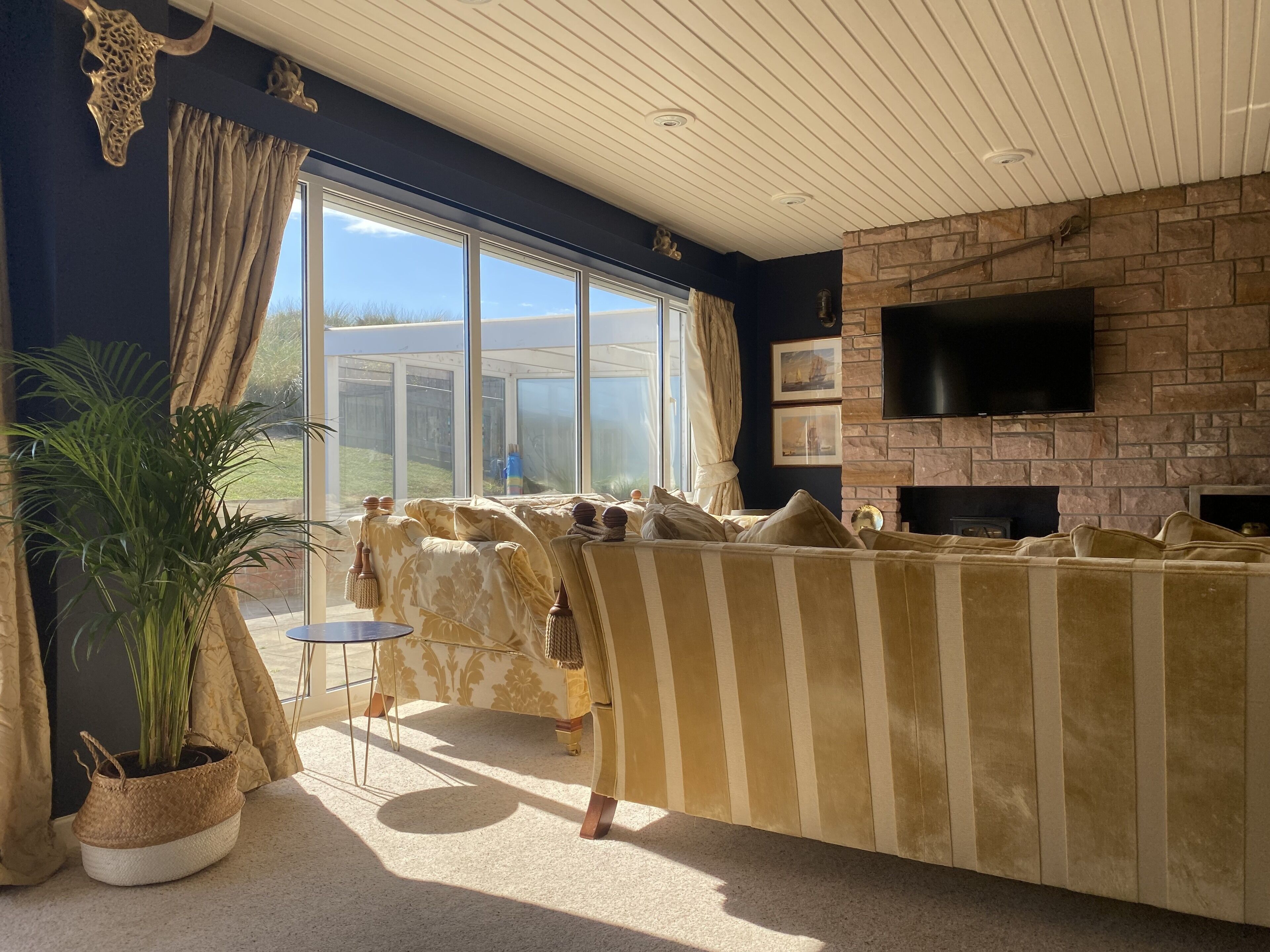A living room with a stone fireplace, large windows, and a striped sofa.