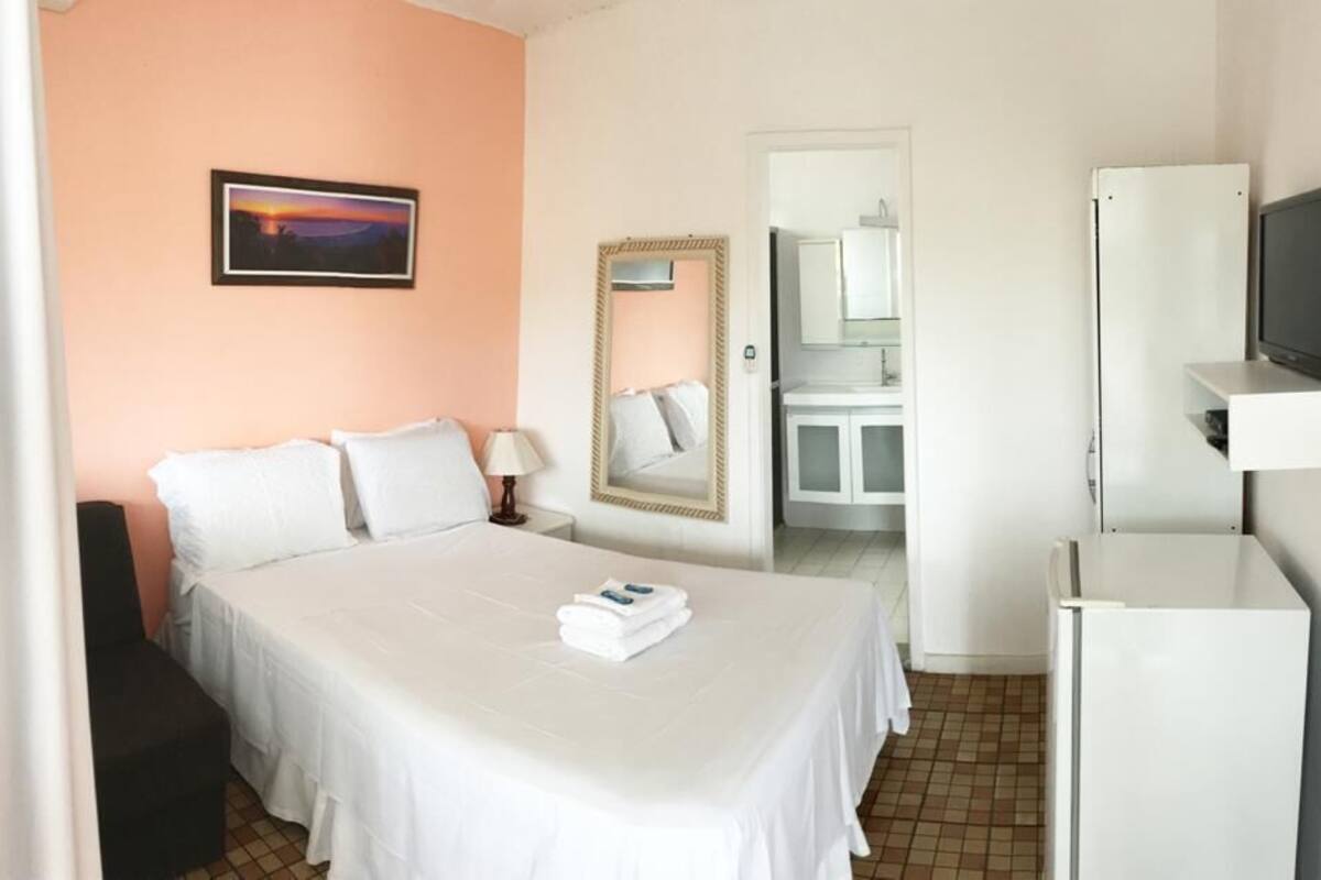 A hotel room with a bed, a television, a mirror, and a door leading to a bathroom.