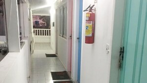 Un couloir au sol carrelé, équipé d’un extincteur et doté d’une porte de couleur turquoise.