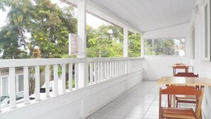 Un espace extérieur abrité, doté d’une rambarde blanche, d’un sol carrelé et d’une table avec des chaises.