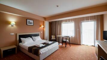 A hotel room with a bed, bedside tables, a desk, a chair, a television, and a window with curtains.