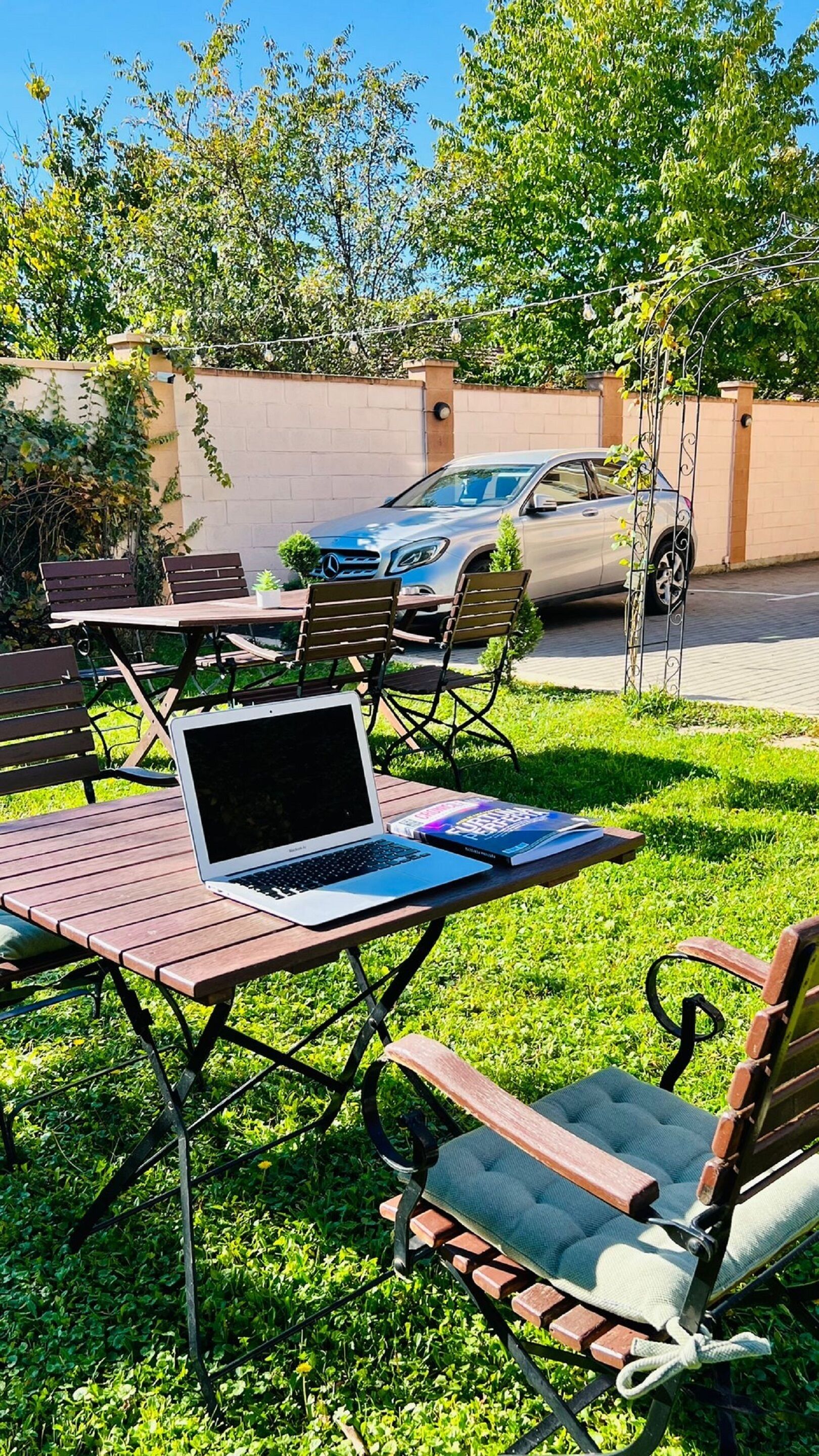 An outdoor seating area with a laptop on a table, surrounded by chairs and a car parked nearby.