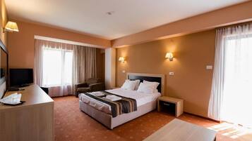 A hotel room with a bed, bedside tables, a desk, a chair, and a television.