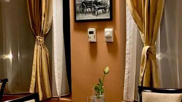 Mesa de jantar posta para dois, com um vaso de flores, copos de vinho e um quadro na parede.