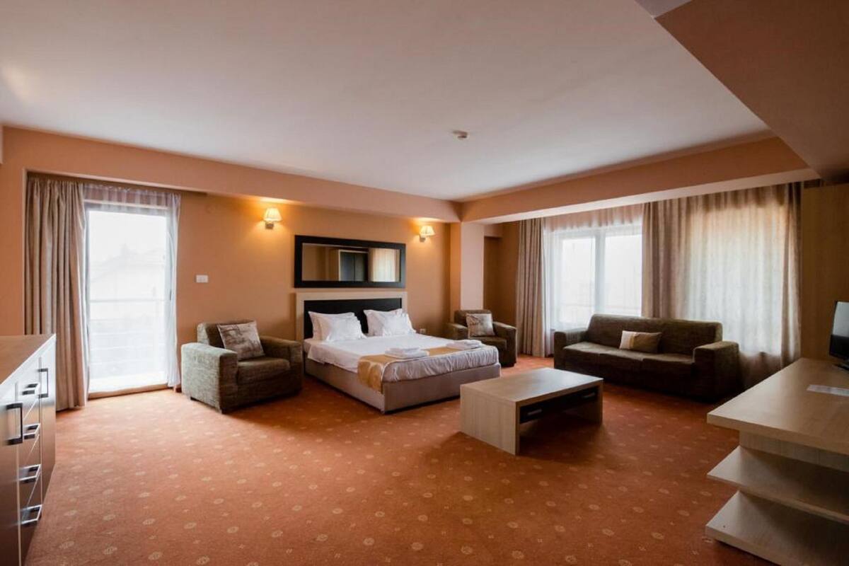 A hotel room with a bed, two armchairs, a sofa, a desk, and a TV.