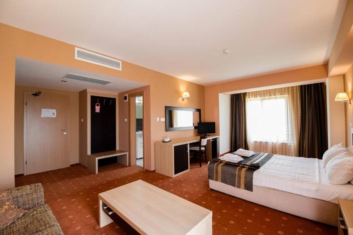 A hotel room with a bed, a desk, a television, a sofa, and a small table.