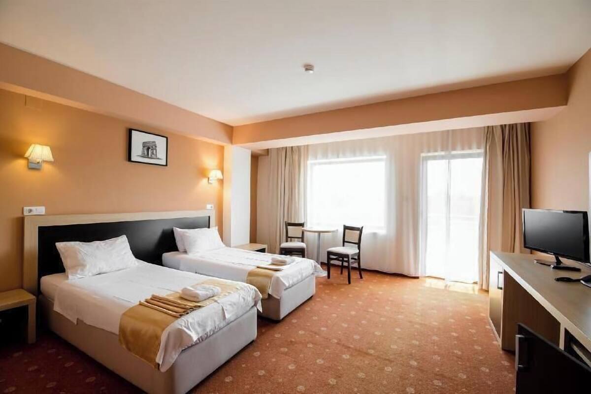 A hotel room with two beds, a desk with a computer, a chair, and a TV.