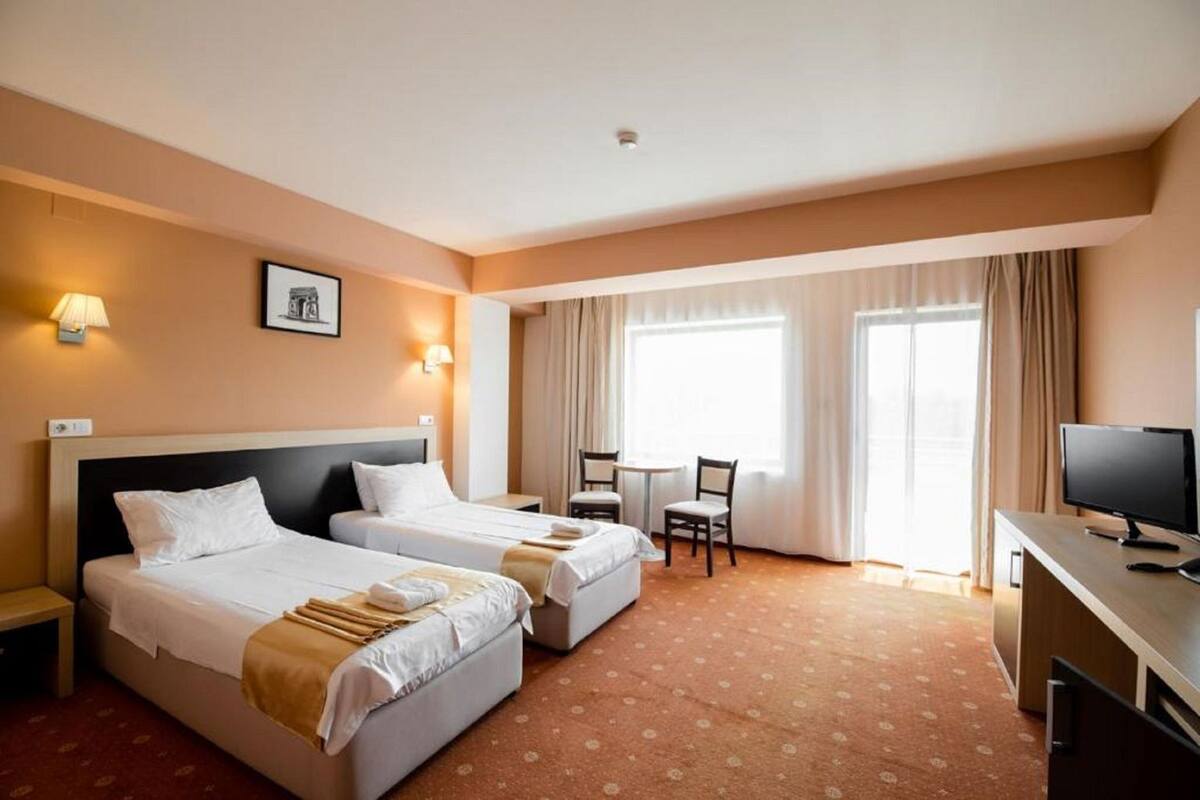 A hotel room with two beds, a desk with a computer, a chair, and a window with curtains.