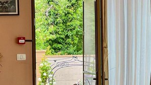 Ein Esszimmer mit gedecktem Tisch, einem Blumenstrauß und Blick auf grüne Bepflanzung durch einen Vorhang.