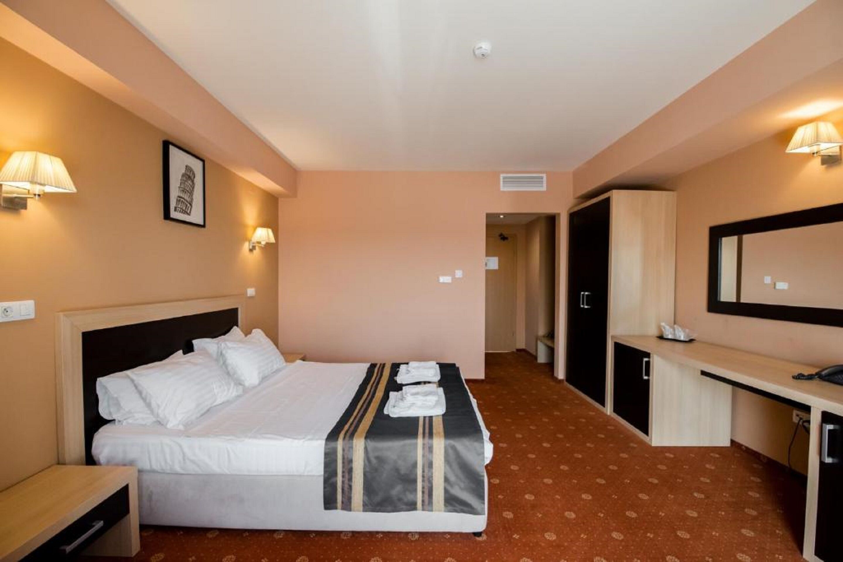 Een hotelkamer met een bed, nachtkastje, bureau en spiegel.