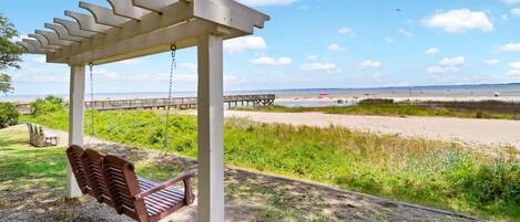 Un columpio de madera bajo una pérgola con vista a una playa y un muelle.