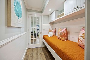 A narrow hallway with a door leading to a room with a bed, a shelf with items, and a wall-mounted artwork.