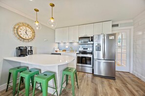 A modern kitchen with a central island, stainless steel appliances, and green bar stools.