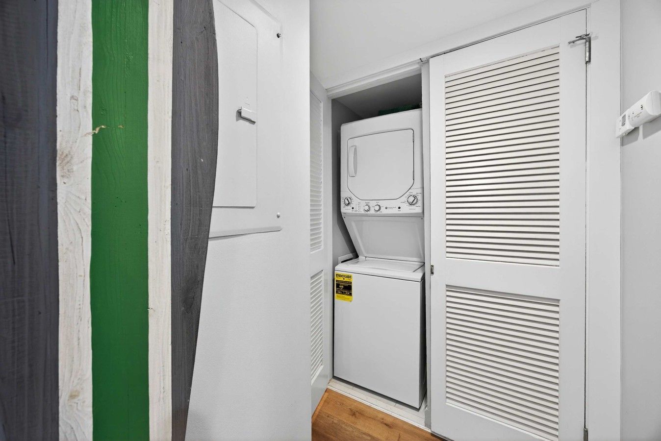 Une buanderie équipée d’un lave-linge et d’un sèche-linge, une porte avec une bande verte et un mur blanc.