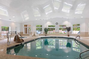 An indoor swimming pool with clear windows, a lifeguard chair, and a clock on the wall.