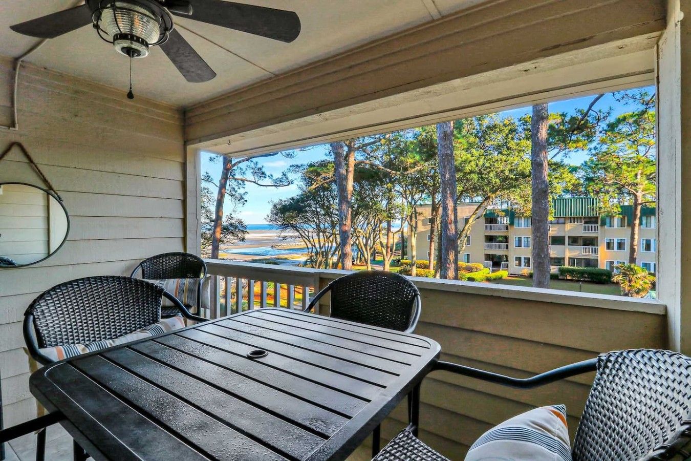 A covered outdoor seating area with a table and chairs, a ceiling fan, and a view of a beach and buildings.