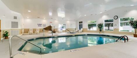 An indoor swimming pool with a clear water surface, surrounded by lounge chairs and a potted plant.